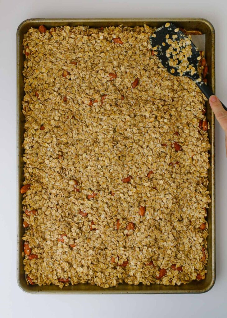packing the wet granola mixture into a baking sheet with a spatula.