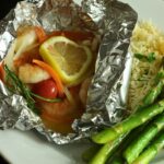 open foil packet with fish and shrimp on a plate.