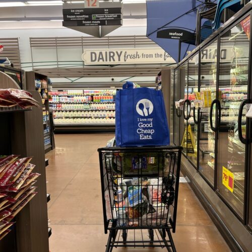 shopping cart in freezer aisle with a good cheap eats shopping bag in the baby seat.