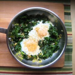 skillet of spinach and eggs on a wood board.