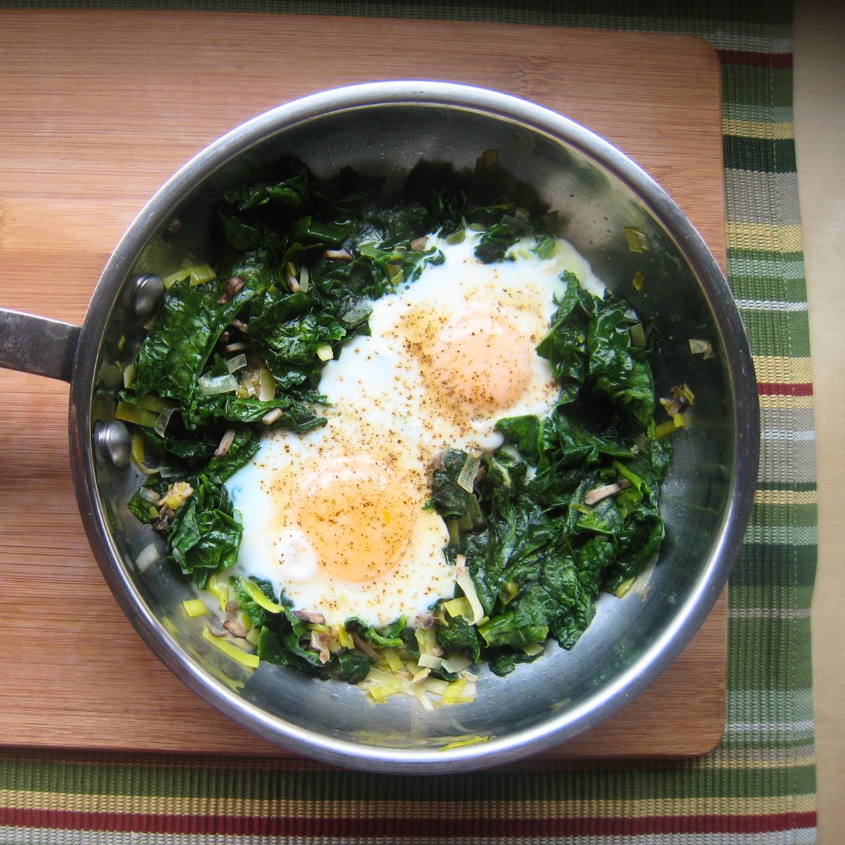skillet of spinach and eggs on a wood board.