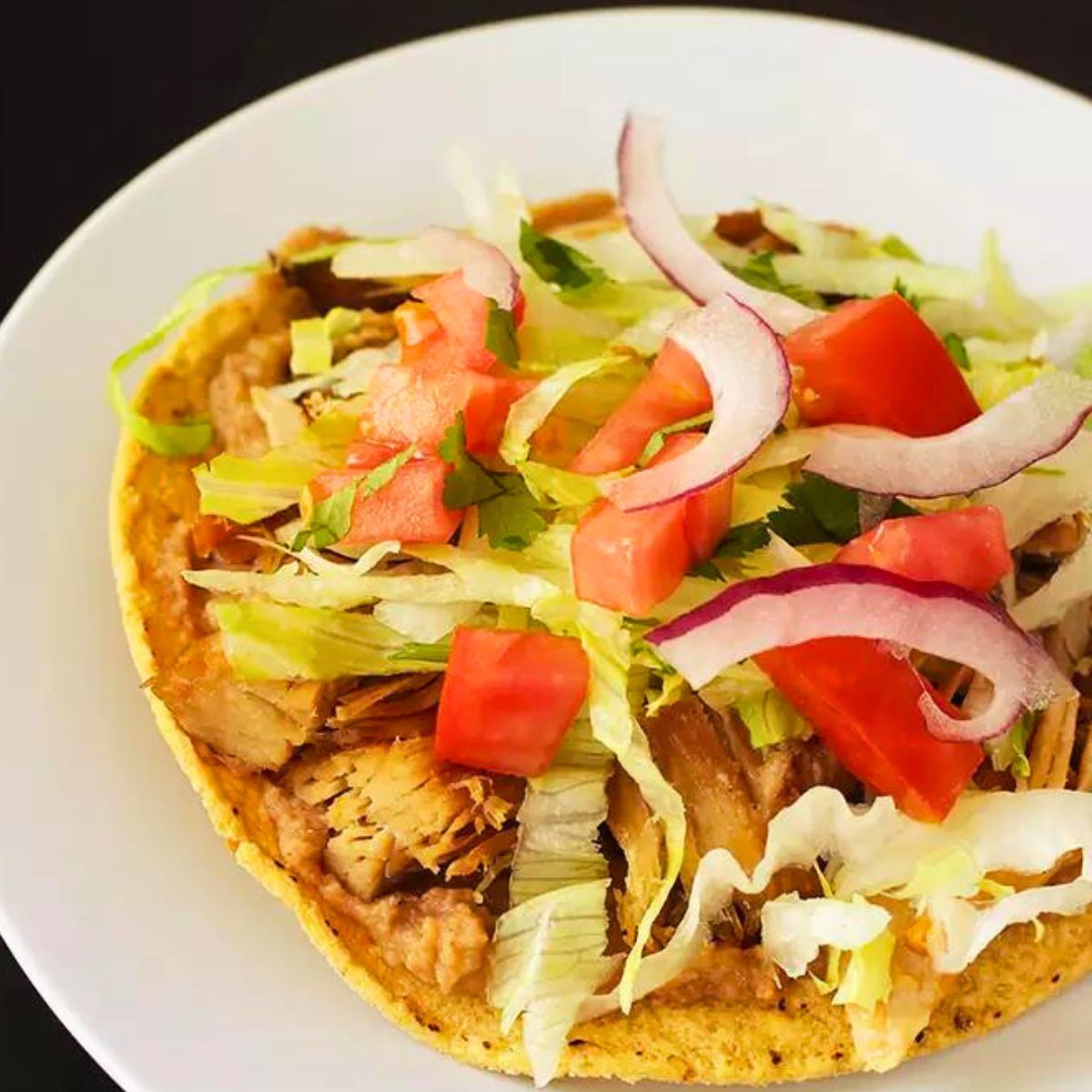 carnitas tostada on white plate on black table.