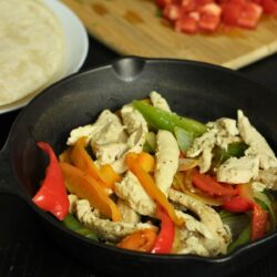 skillet of chicken fajitas on table with tortillas and toppings.