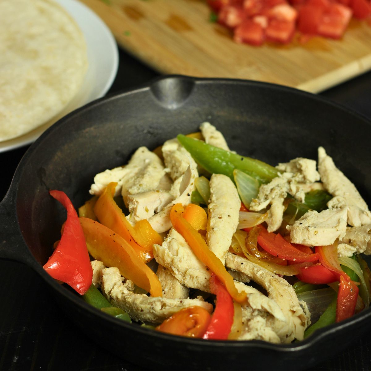 skillet of chicken fajitas on table with tortillas and toppings.