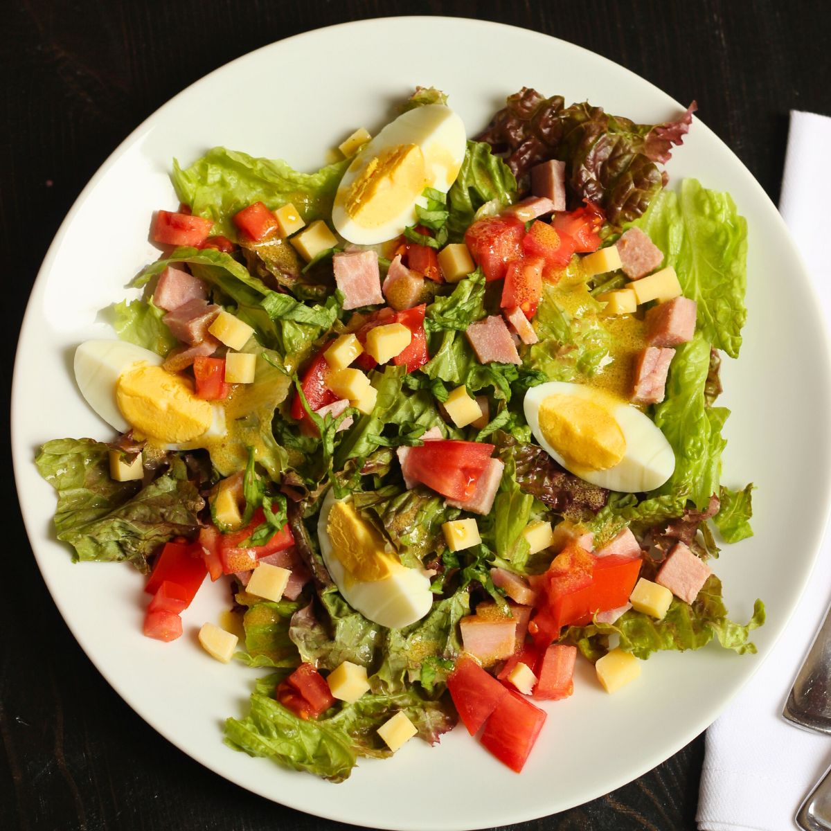 overhead shot of ham and cheese salad with french vinaigrette dressing drizzled over top.