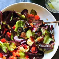 tossed italian salad in white bowl with Peligrino nearby