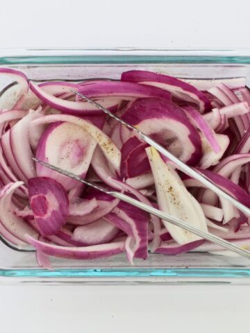 square crop of red pickled onions in glass dish with tongs.