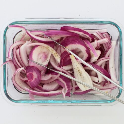 square crop of red pickled onions in glass dish with tongs.