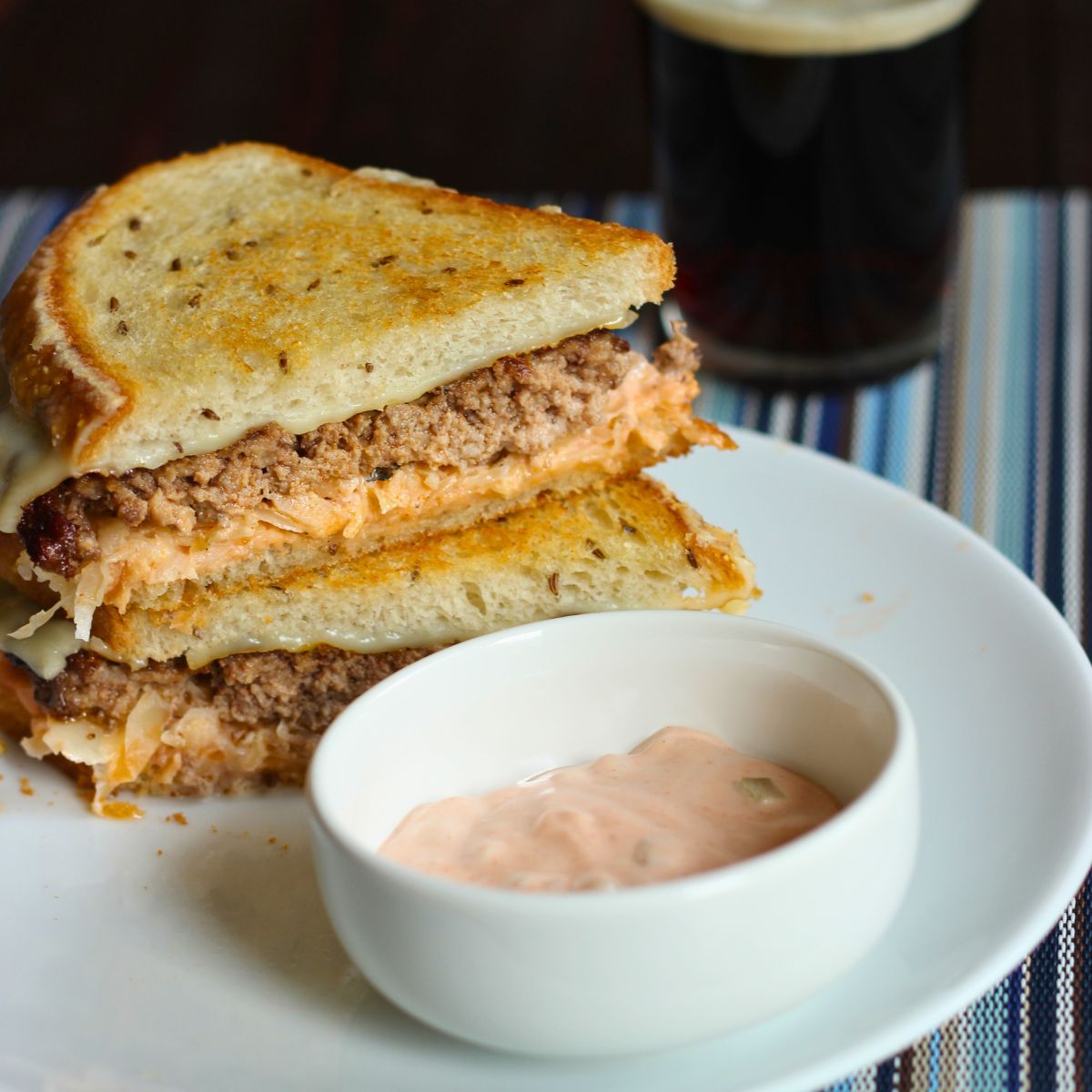 two halves of a reuben patty melt stacked on a plate with dish of 1000 island dressing.