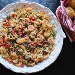 white bowl of pasta topped with shrimp and fresh cilantro.