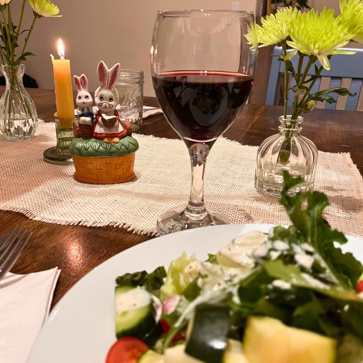 ceramic bunnies on table runner with wine glass and dinner plate in the foreground.