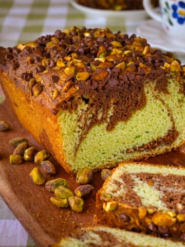 chocolate pistachio loaf sliced on a board with nuts nearby.