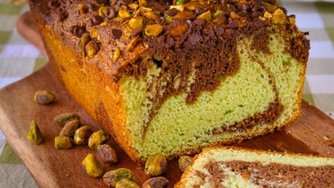 chocolate pistachio loaf sliced on a board with nuts nearby.