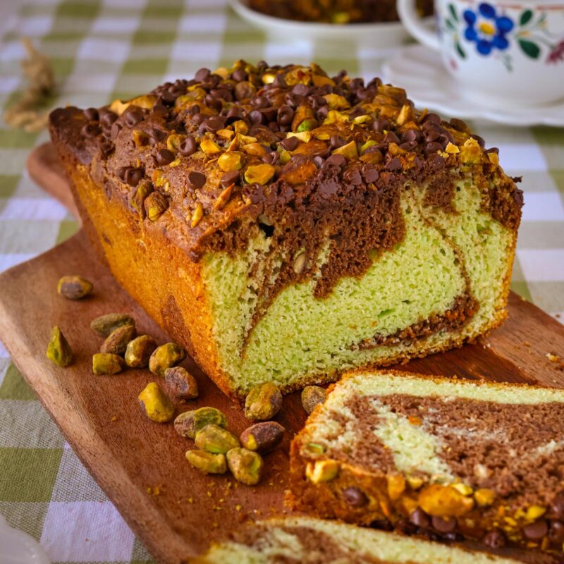 chocolate pistachio loaf sliced on a board with nuts nearby.
