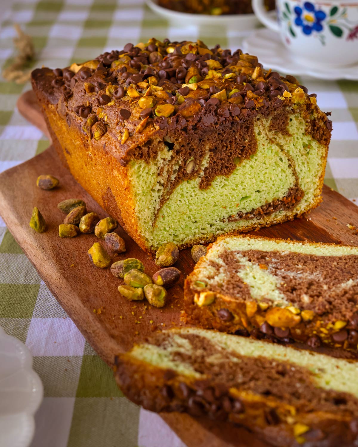 chocolate pistachio loaf cake sliced on a wooden board on a tea table.