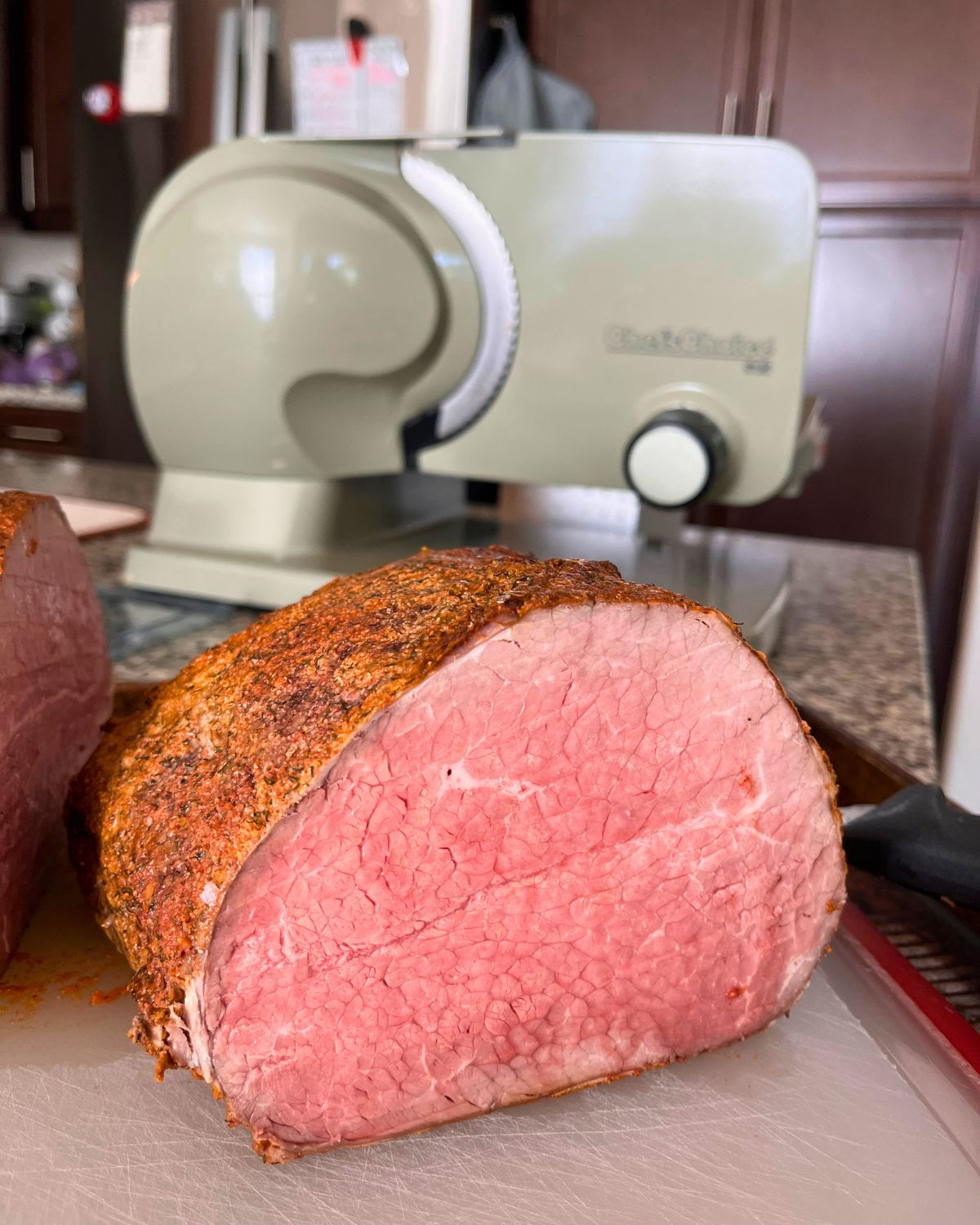 roast cut in half on cutting board in front of meat slicer.
