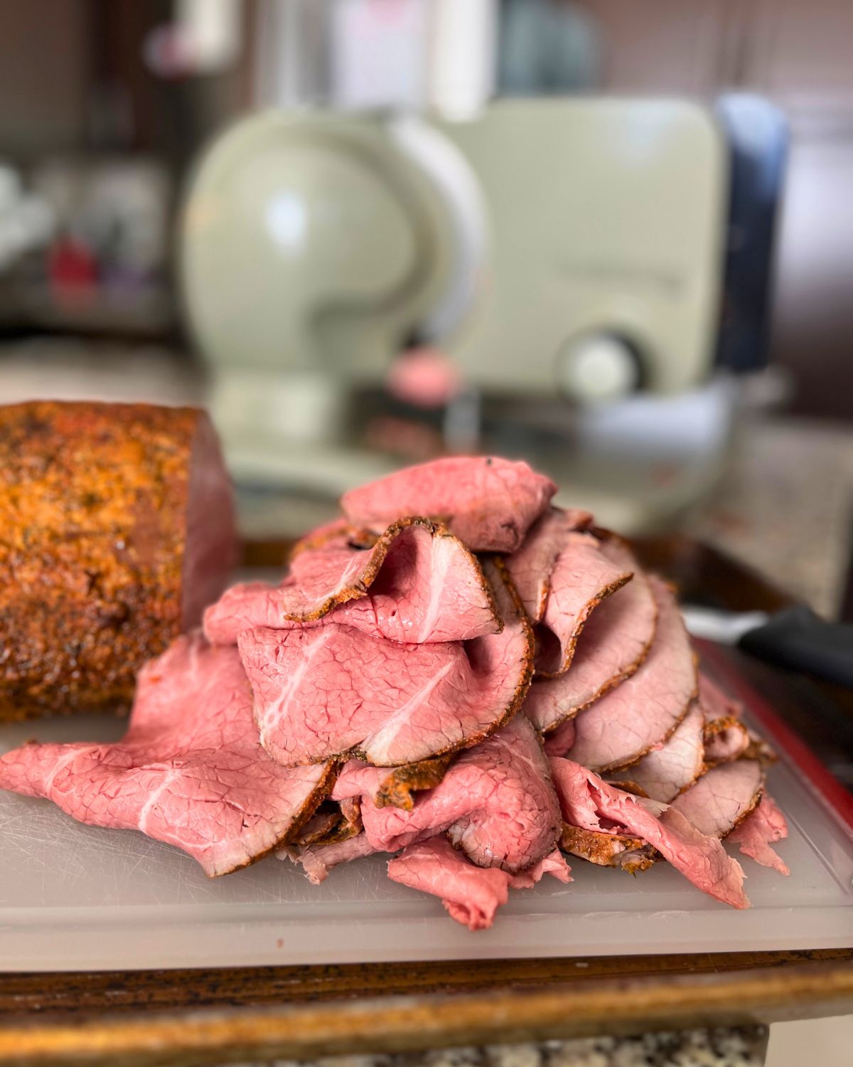 roast beef sliced in a pile on the cutting board near meat slicer.