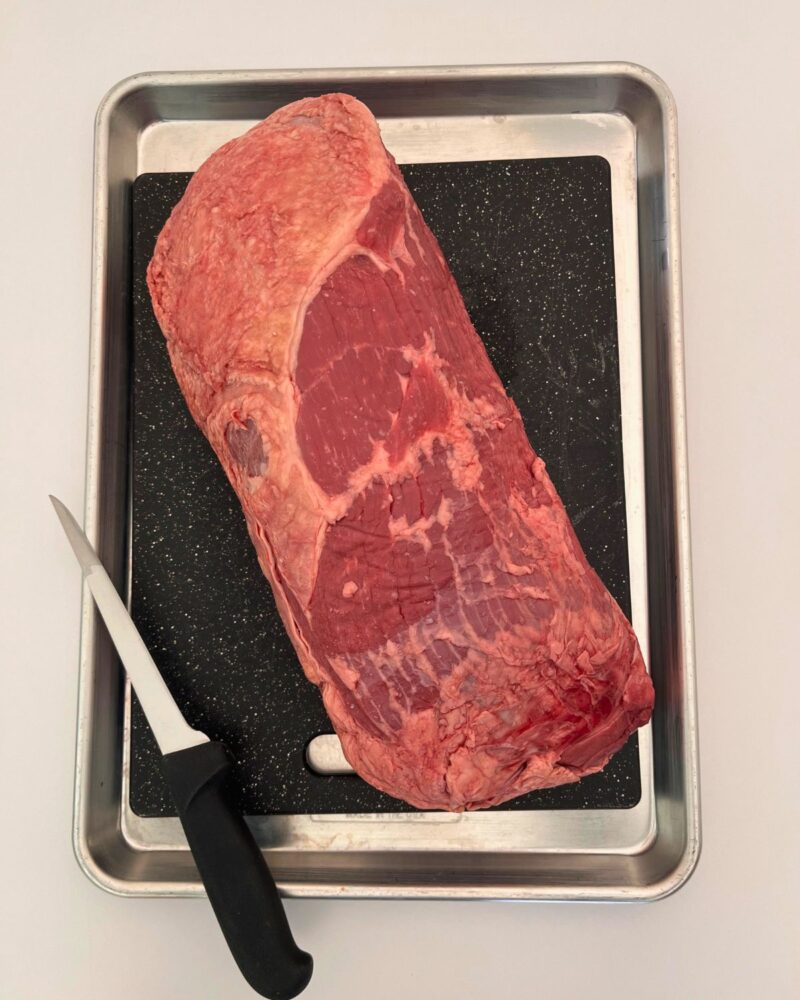 untrimmed roast on cutting board set inside sheet pan.