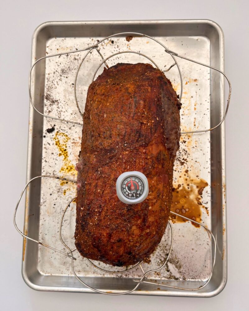 cooked roast on racks in sheet pan with meat thermometer reading at 130 degrees.